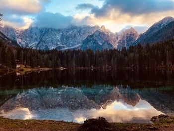 Scenic view of lake and snowcapped mountains against cloudy sky during sunset