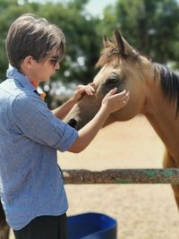 Young man stroking horse in animal pen