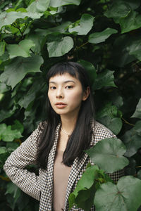 Portrait of beautiful young woman standing against plants