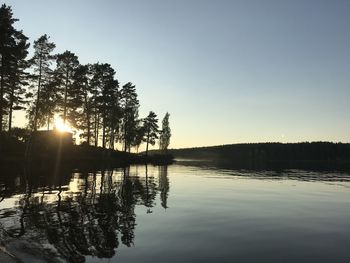 Silhouette trees by lake against sky during sunset