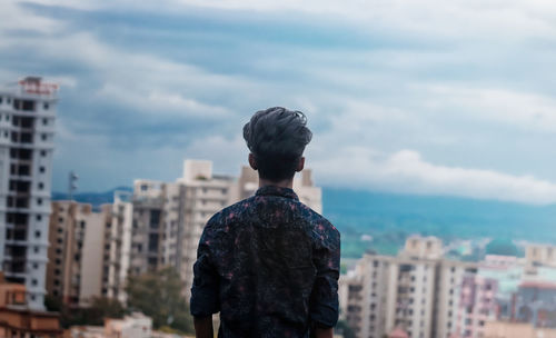 Rear view of man looking at city buildings against sky