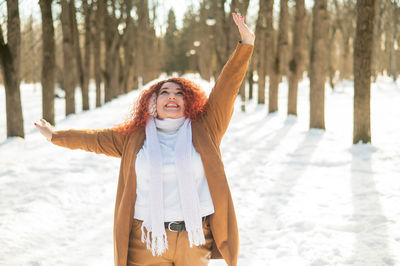 Portrait of young woman with arms outstretched standing on snow covered field