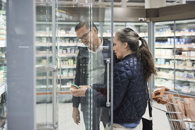 Couple looking at food container in refrigerated section of supermarket