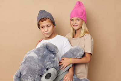 Sibling with stuffed toy against beige background