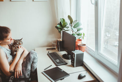 Side view of woman playing with cat while sitting by desk at home