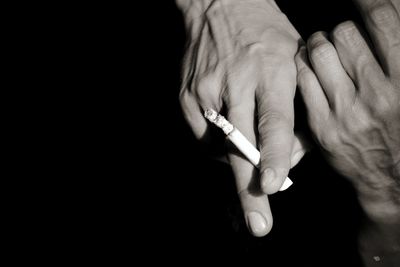 Cropped hands holding cigarette against black background