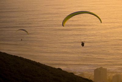 Silhouette person paragliding over sea against sky during sunset