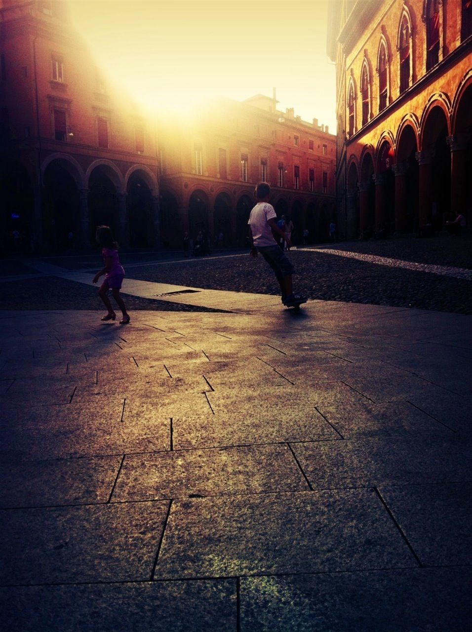 building exterior, architecture, built structure, lifestyles, full length, city, street, leisure activity, men, walking, city life, sunlight, person, building, cobblestone, outdoors, sunset, incidental people