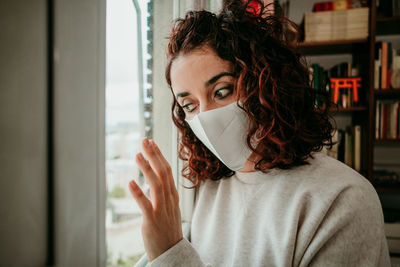 Close-up of woman wearing mask looking through window at home