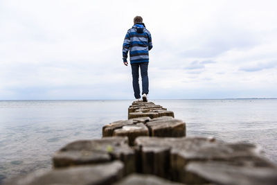 Rear view of man standing at sea shore against sky