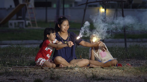 Family holding sparklers while sitting on field