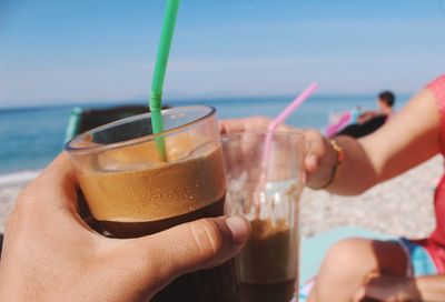 Midsection of woman holding drink at beach against clear sky
