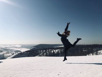 Woman jumping on snow covered field against sky
