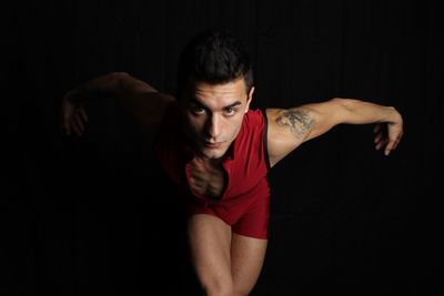 Portrait of young handsome man dancing with arms outstretched against black background