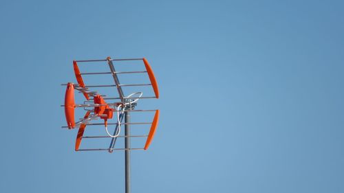 Low angle view of red television aerial against clear blue sky