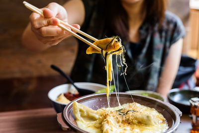 Gyoza with melt cheese raised by chopsticks on woman hand. traditional japanese food in restaurant.