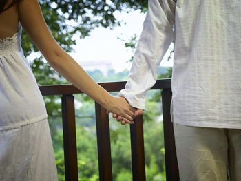 Midsection of couple with holding hands standing against trees