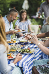 Woman serving food while sitting with friends and family at backyard during weekend party