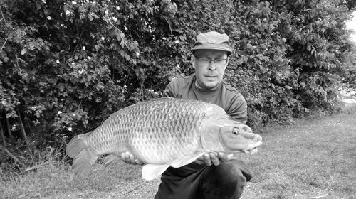 Man holding fish while kneeling against plants