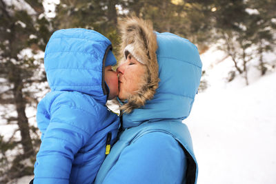 Woman kissing son while standing on snowy field