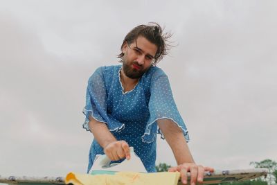 Low angle view of man wearing dress ironing laundry against sky