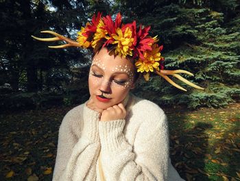 Young woman with makeup sitting against plant