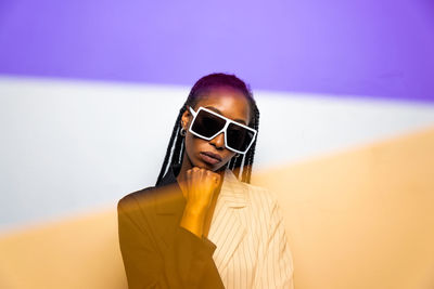 Portrait of young woman wearing sunglasses standing against wall