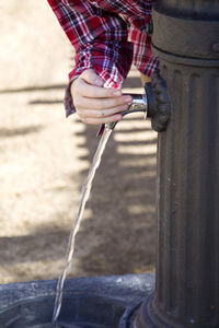 Cropped hand pressing faucet with running water