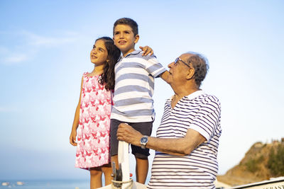 Grandfather with grandchildren on boat against sky