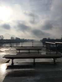 Empty bench by lake against sky