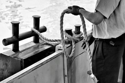 Midsection of man holding rope while standing in boat