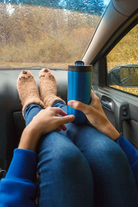 Low section of woman holding bottle sitting in car