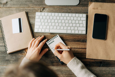 Midsection of woman using mobile phone by laptop on table