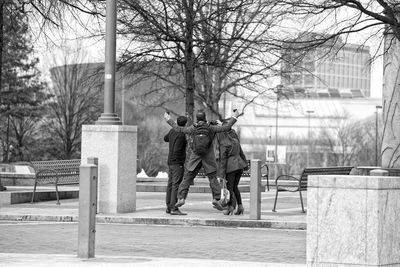 Rear view of man jumping by friends on footpath