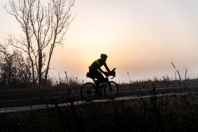 Silhouette person cycling on road against sky