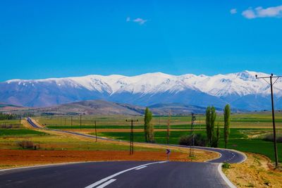 Road leading towards mountains against blue sky