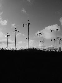 Low angle view of silhouette windmills on field against sky