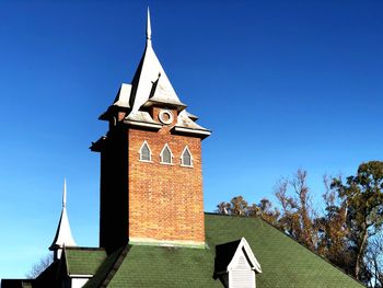 Low angle view of clock tower amidst buildings against clear blue sky