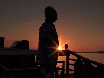 Silhouette man standing by railing against sky during sunset