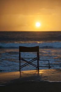 Lifeguard chair on beach against sky during sunset