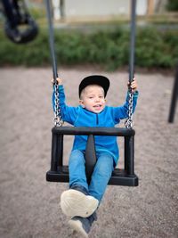 Portrait of cute boy sitting on swing at playground