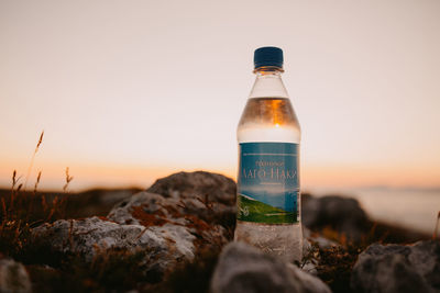 Close-up of water bottle on rock against sky during sunset