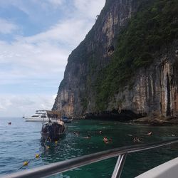 People swimming by boat in sea against mountain