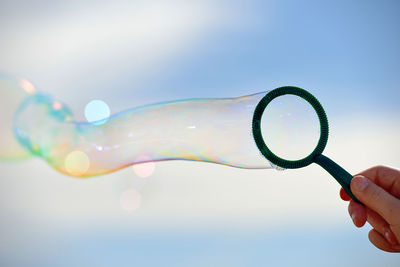 Cropped hand of person holding bubble wand against sky