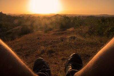 Low section of man sitting on landscape against clear orange sky