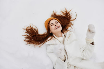 Smiling young woman lying on snow covered land