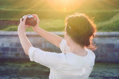 Rear view of girl taking a selfie by canal