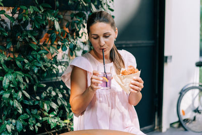 A woman sitting at a table in a street cafe eats a sandwich.