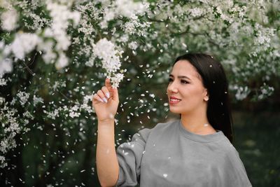 Portrait of a smiling beautiful young woman against white flowering plants