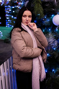 Portrait of young woman standing by christmas tree